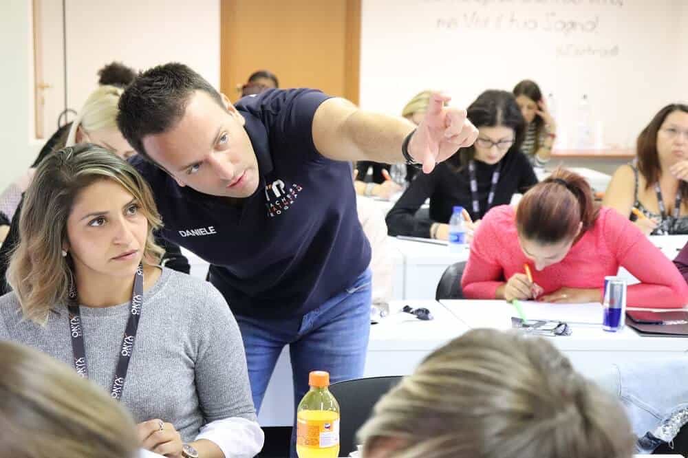 Daniele Salamina in aula che spiega a un'allieva, con la classe al lavoro