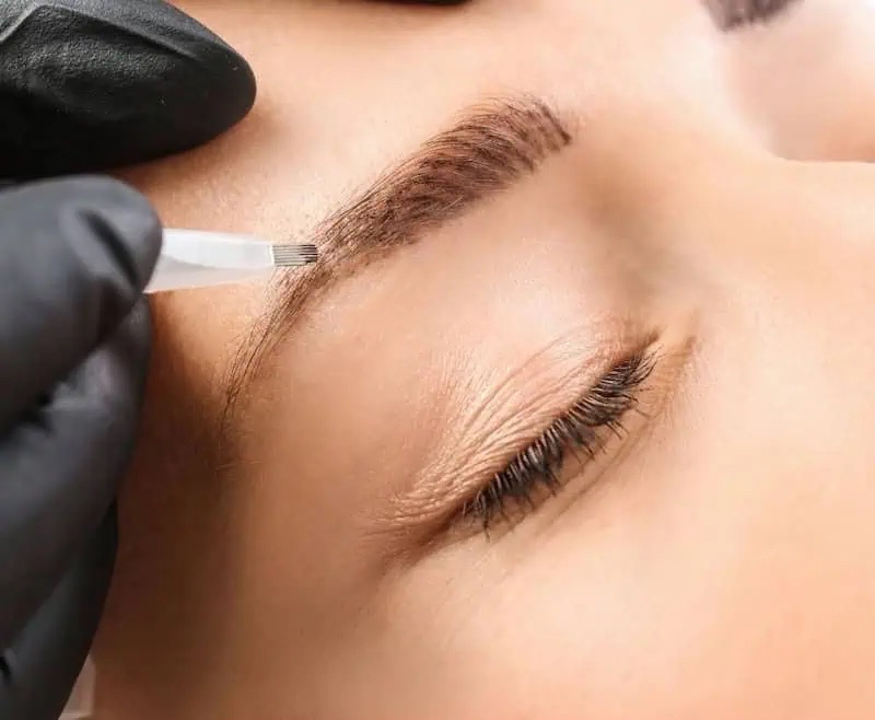 Mano con il guanto nero che disegna i peli del sopracciglio con la penna da microblading